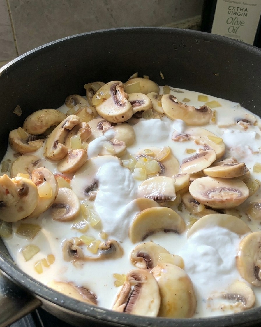 A person tasting a white cream sauce with a small spoon from a black skillet containing mushrooms.