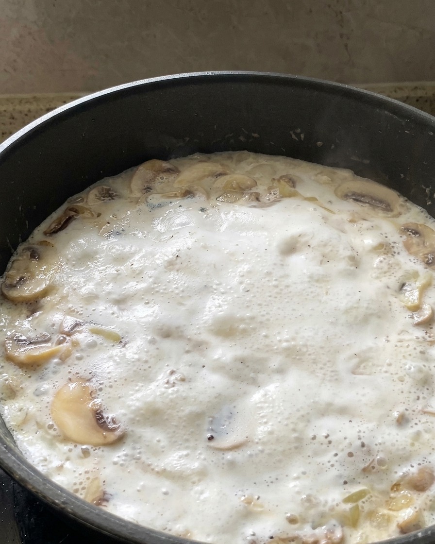 Fresh green spinach leaves being added to a bubbling white mushroom cream sauce in a pan.