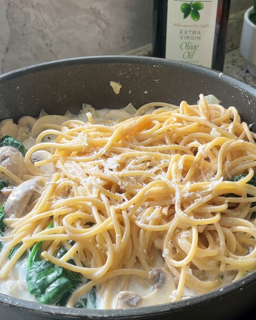 Fine shreds of parmesan cheese scattered over a pan of creamy mushroom and spinach spaghetti.
