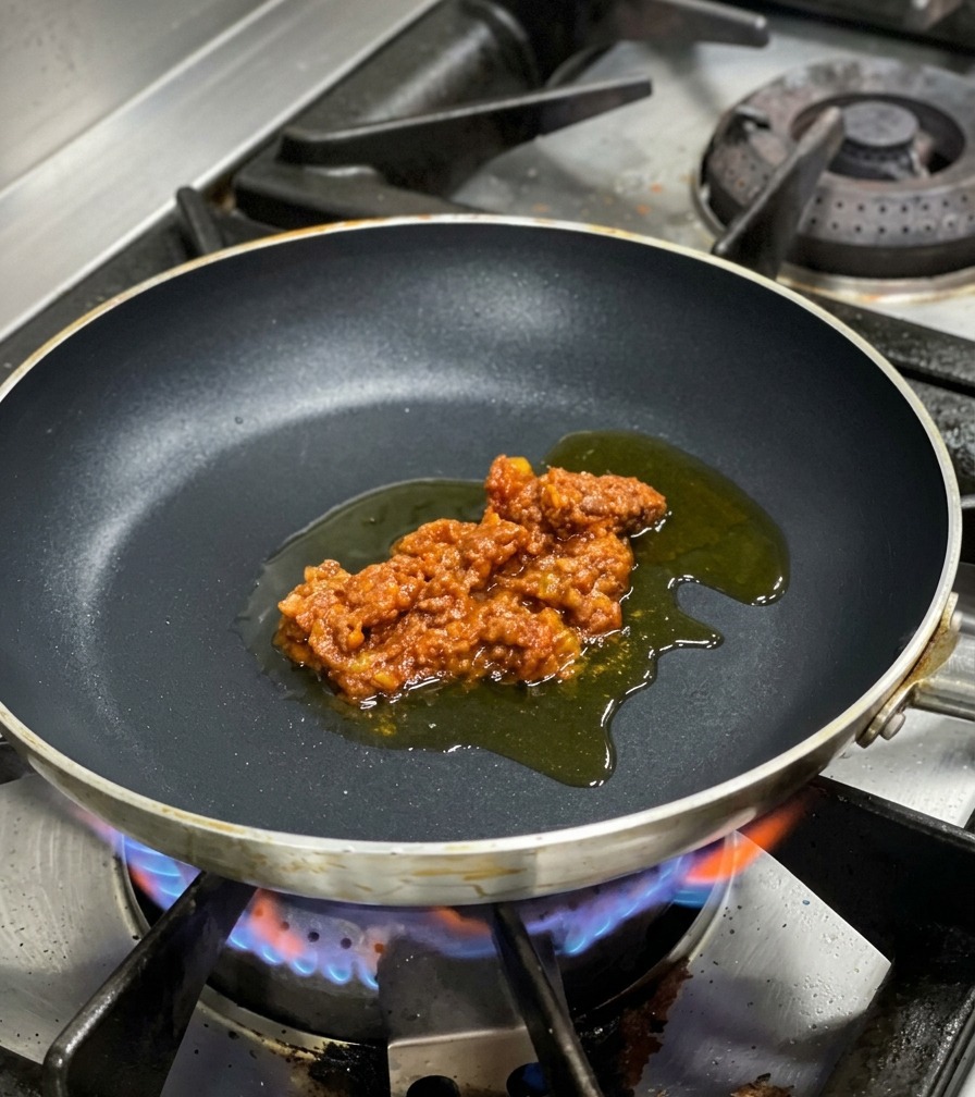 A thick mound of red meat sauce sitting in olive oil in the middle of a frying pan on a stove.