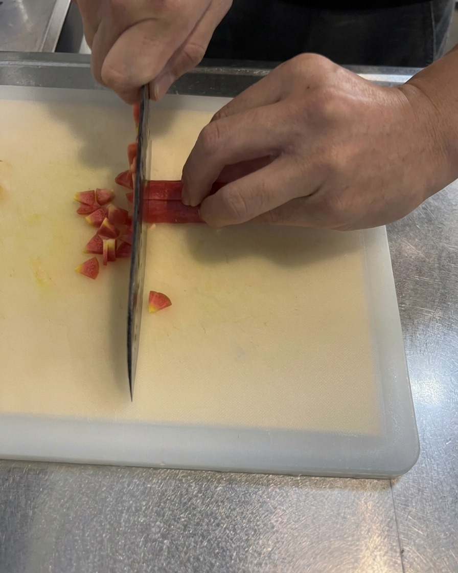 Hands dicing a bright carrot into small, even squares on a white cutting board using a kitchen knife.