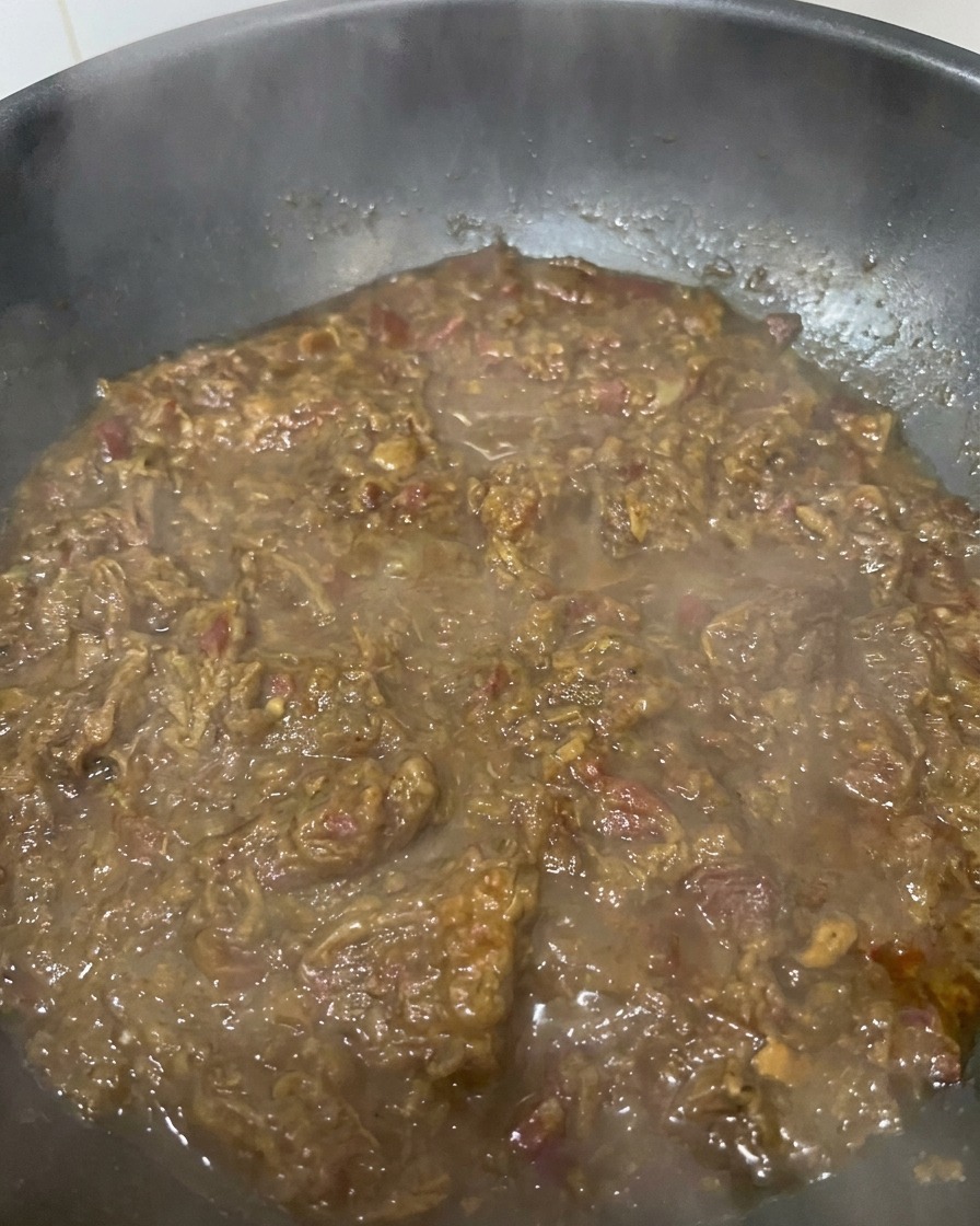 A close-up of a thick, dark brown onion and beef sauce simmering in a pan, showing a rich and jammy texture.