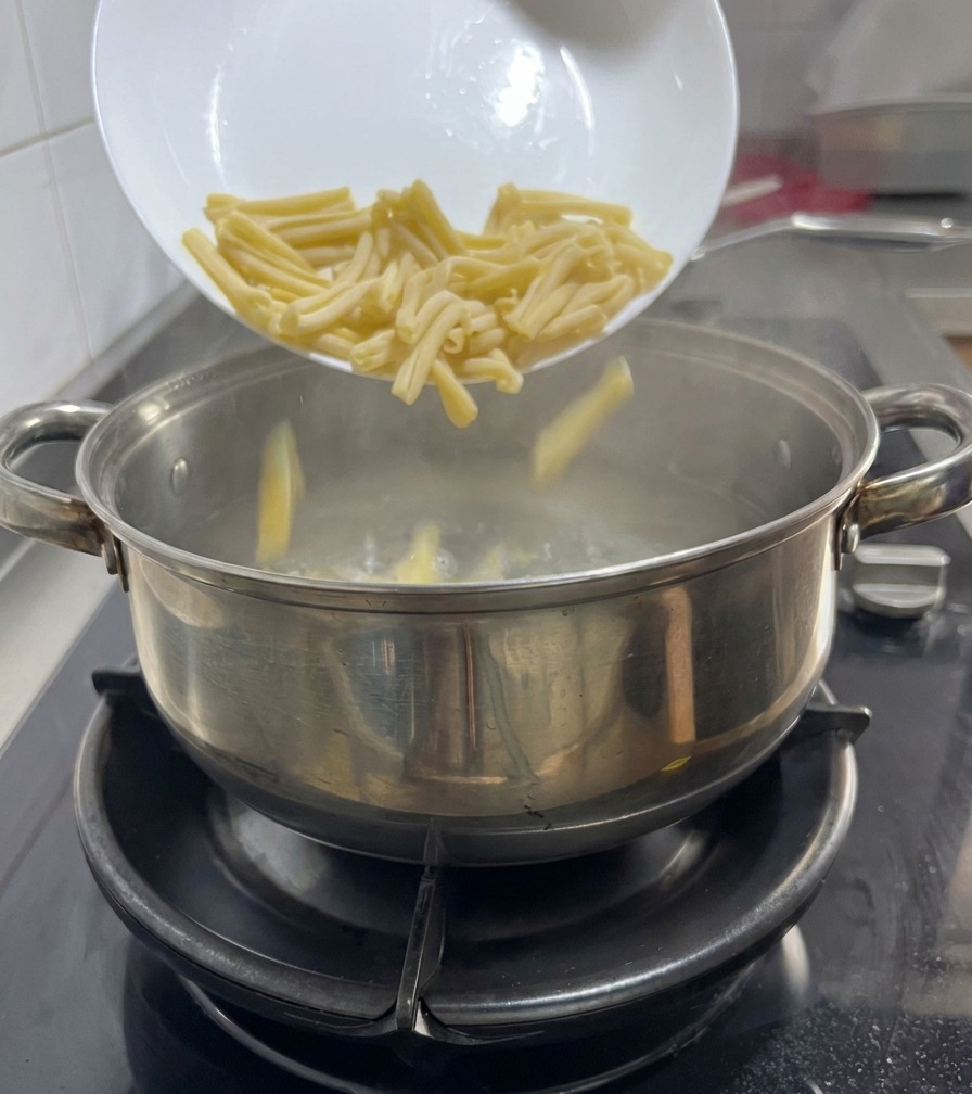 Casarecce pasta being poured from a white plate into a pot of boiling water on a gas stove.