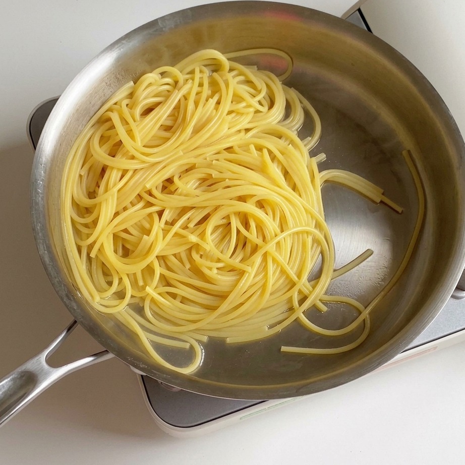 A top-down view of cooked, drained spaghetti in a stainless steel pan with a small cube of yellow butter melting in the center.