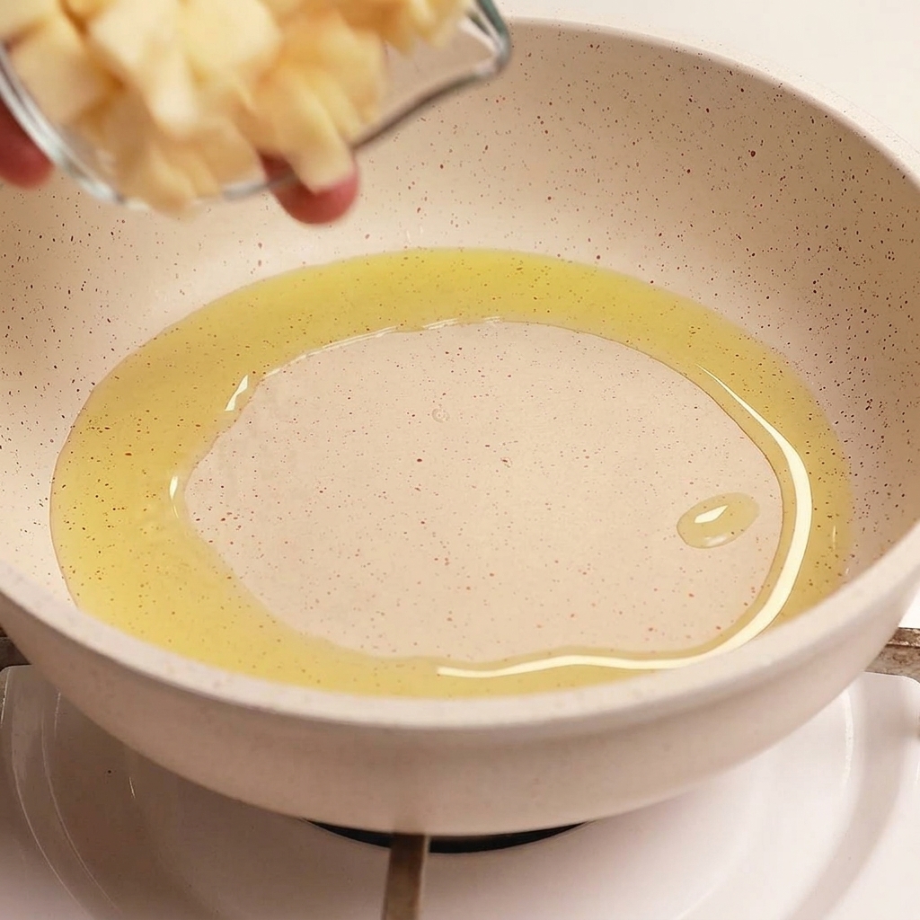 A small glass bowl pouring thin, uniform slices of fresh garlic into a pan containing hot, shimmering olive oil.
