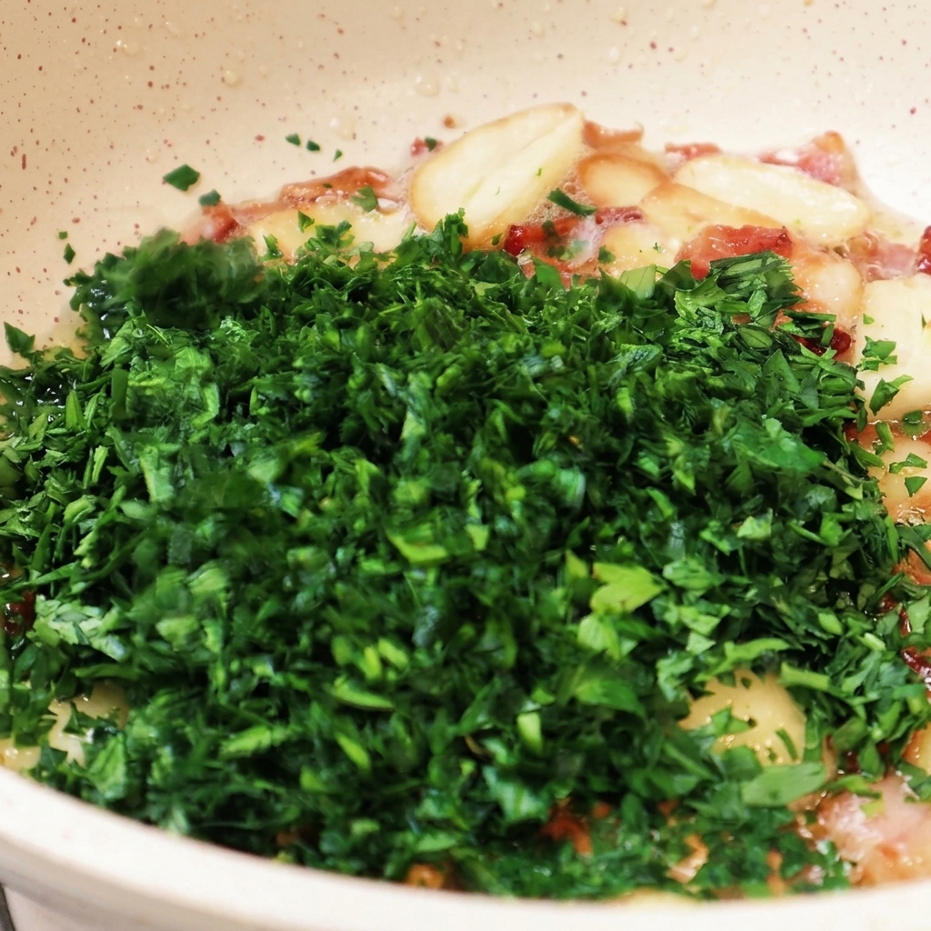 A large mound of finely minced green parsley being added to a pan containing fried garlic and bacon pieces.