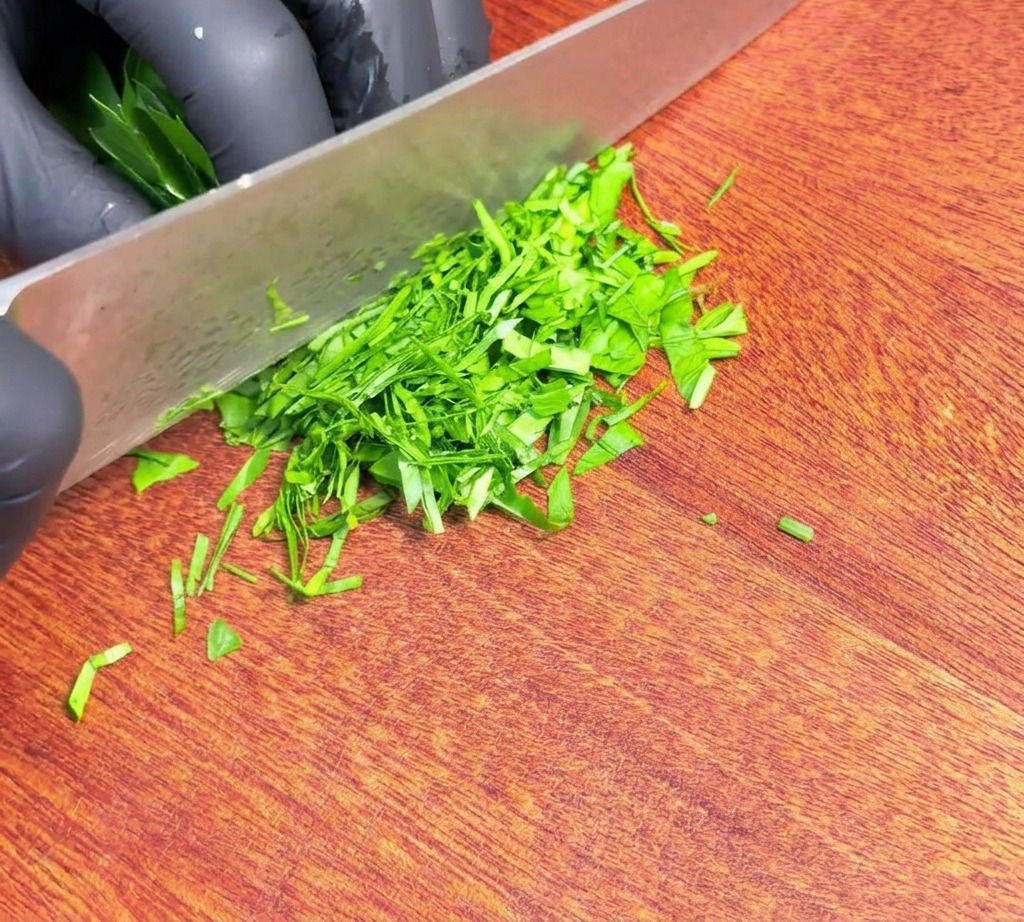 Finely chopped fresh green parsley spread across a wooden cutting board next to the blade of a sharp knife.