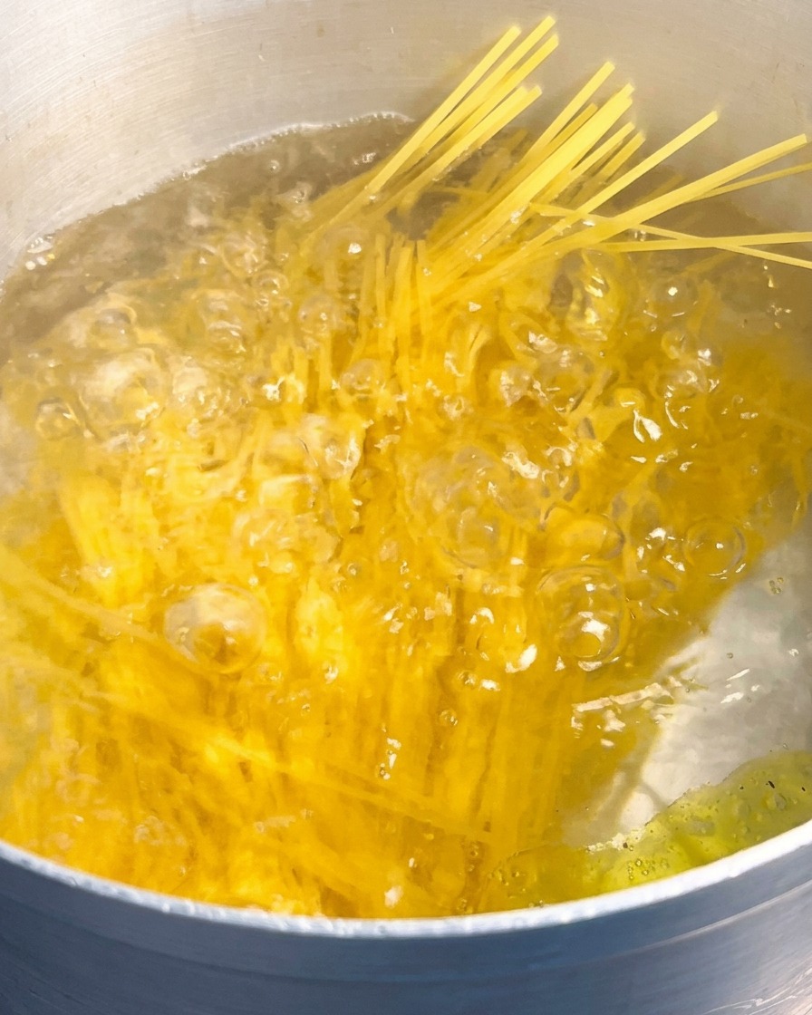 A bundle of yellow dry spaghetti being submerged in a large pot of rapidly boiling water.