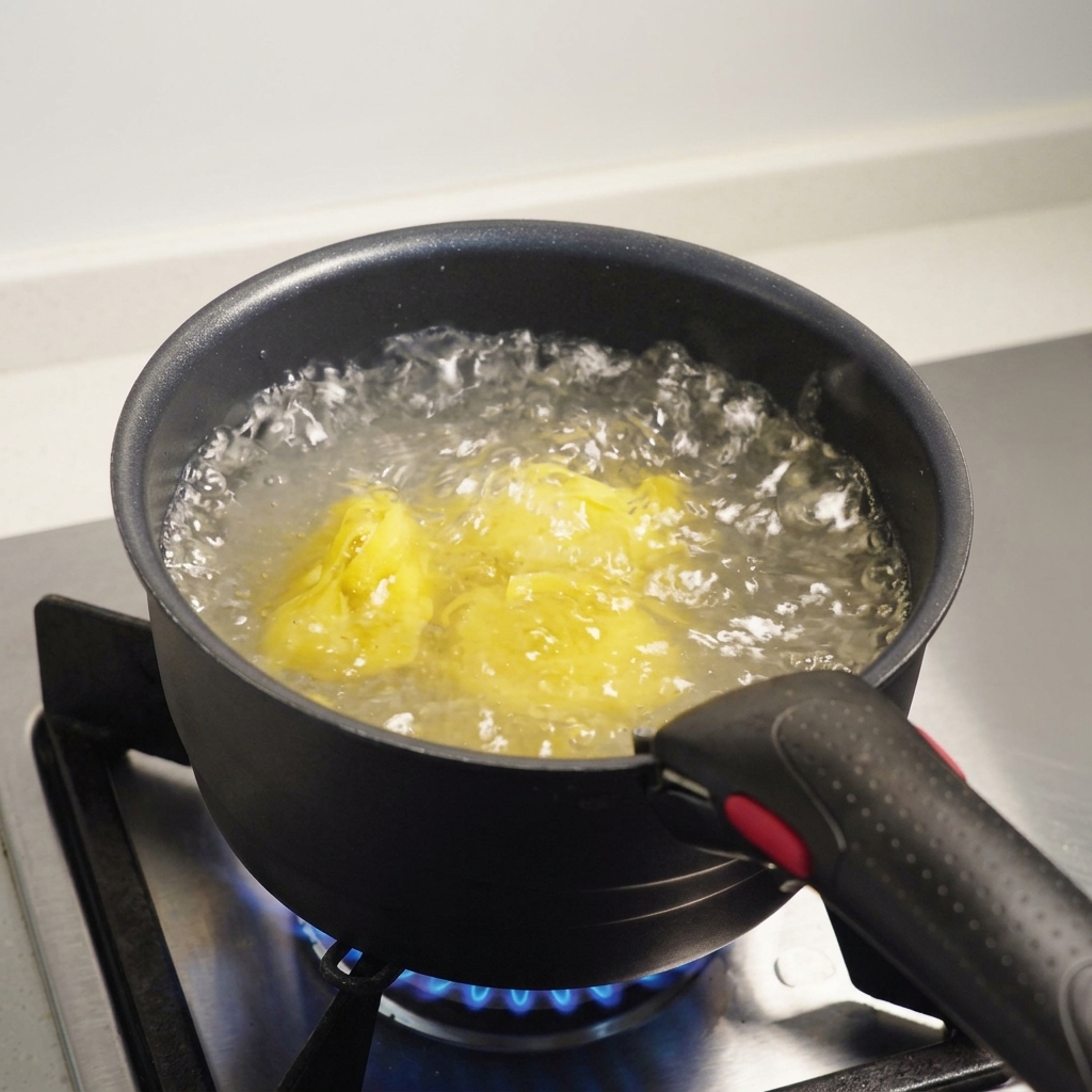 Fettuccine pasta submerged in boiling, salted water inside a dark pot on a gas stove.