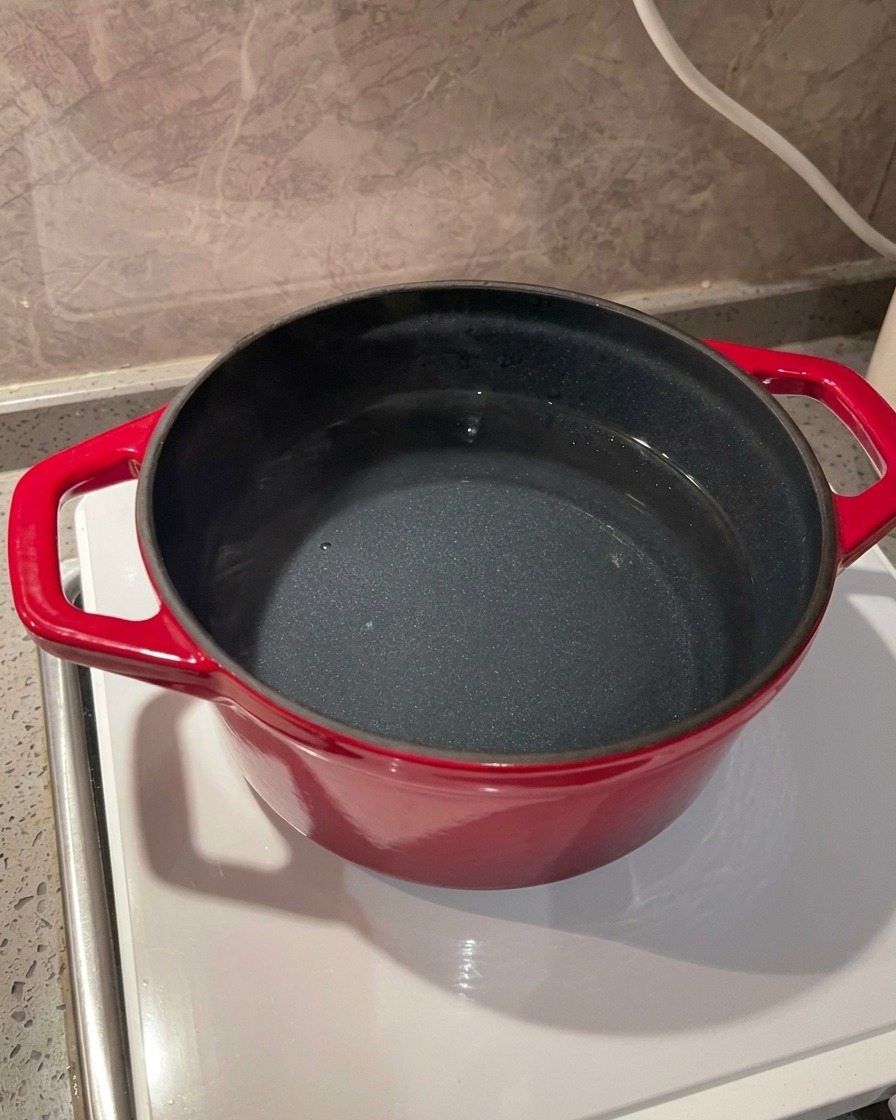 A close-up of sea salt being poured into a vibrant red pot filled with water on a sleek induction stove.