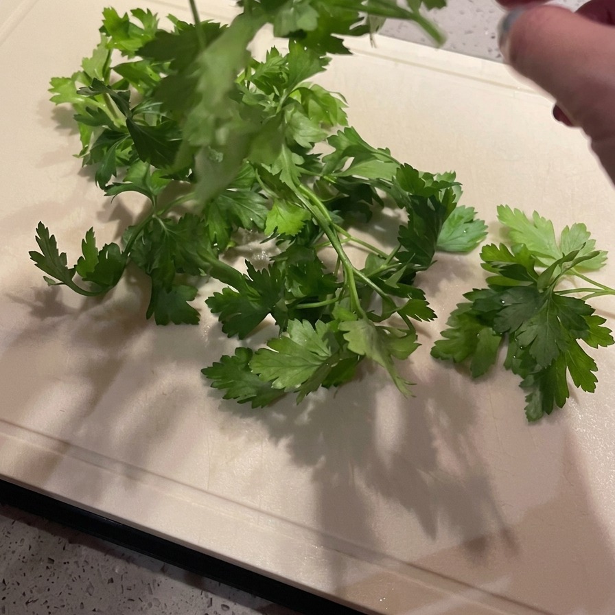 Hands removing vibrant green parsley leaves from their stalks over a light-colored cutting board.
