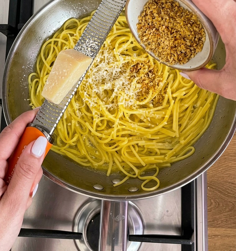 A block of Parmesan cheese being grated with a microplane over a pan of yellow noodles.