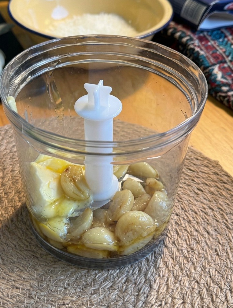 Roasted garlic cloves and a block of butter inside a small transparent blender cup placed on a woven mat.