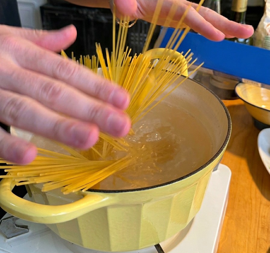 A person submerging a bundle of dry spaghetti into a yellow pot filled with boiling water.