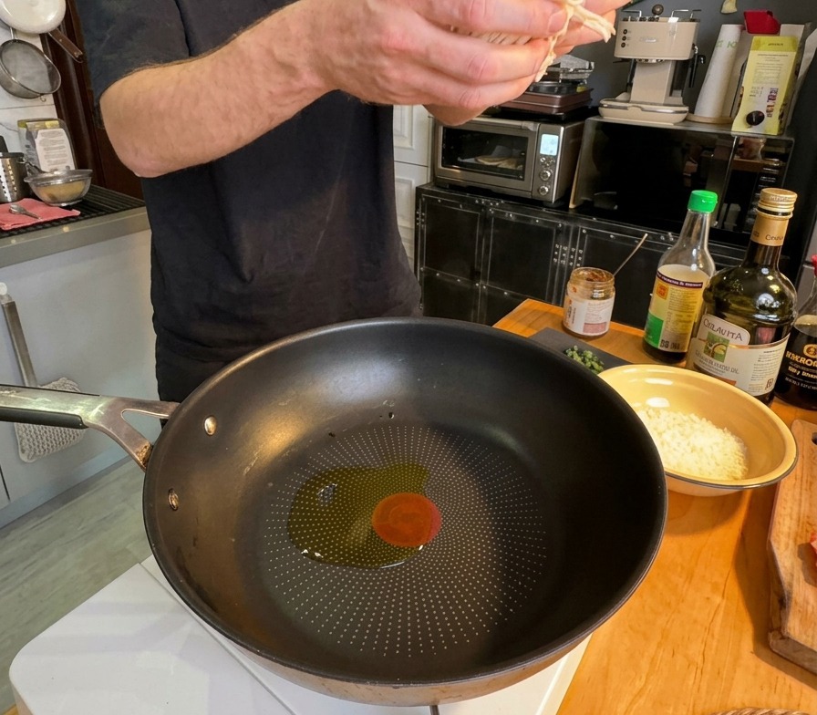 A person adding a handful of sliced white onions into a pan with shimmering olive oil.