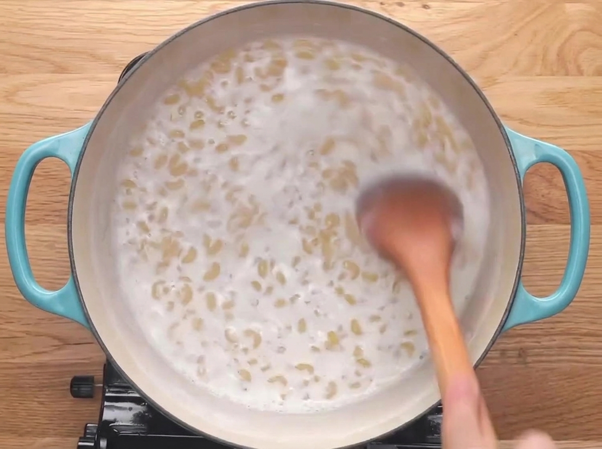 A wooden spoon stirring elbow pasta as it simmers in milk.