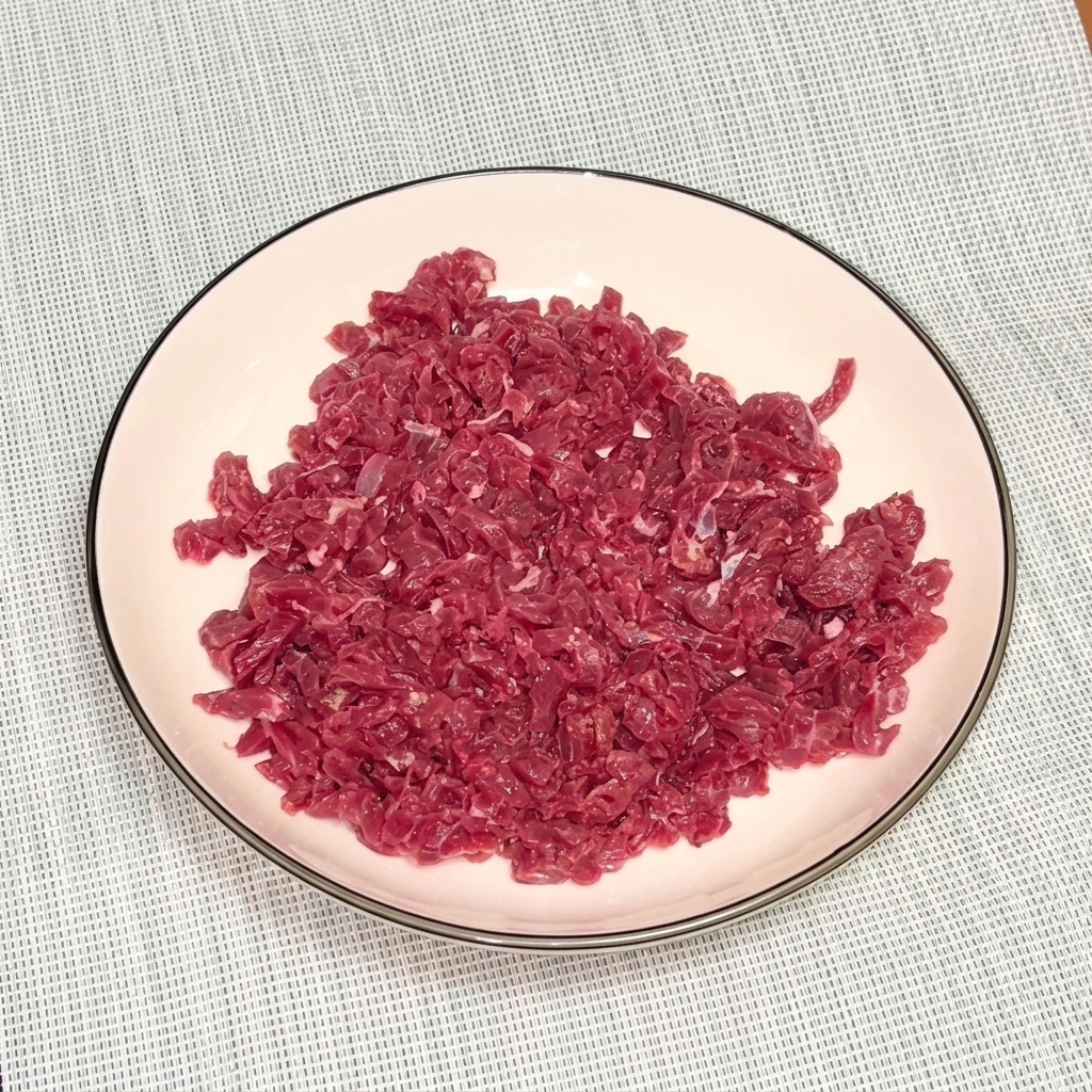 Raw minced beef in a white bowl topped with black pepper and oil for marination.