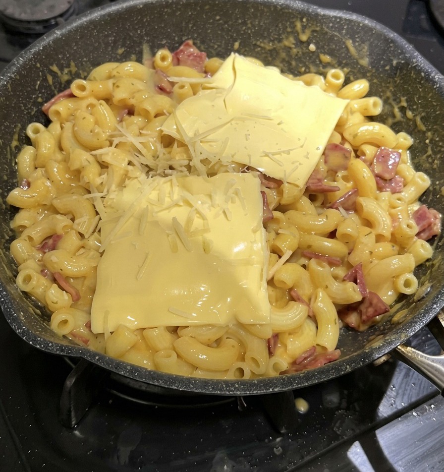Two yellow square cheese slices and shredded cheese sitting on top of a pan of macaroni and cheese.