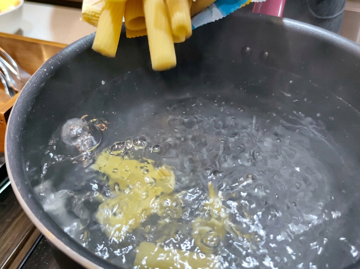 Yellow dry Rigatoni pasta being dropped into a pot of bubbling, boiling water.