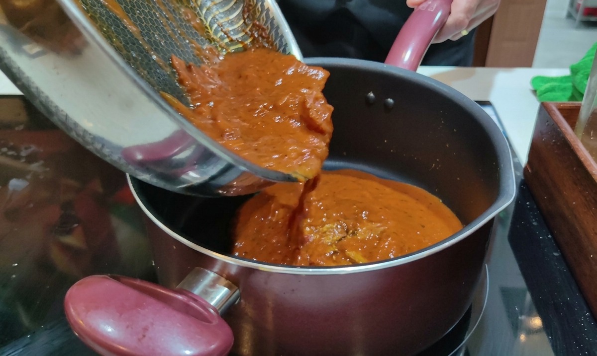 Pouring cooked red Amatriciana sauce from a frying pan into a pot of boiled Rigatoni.
