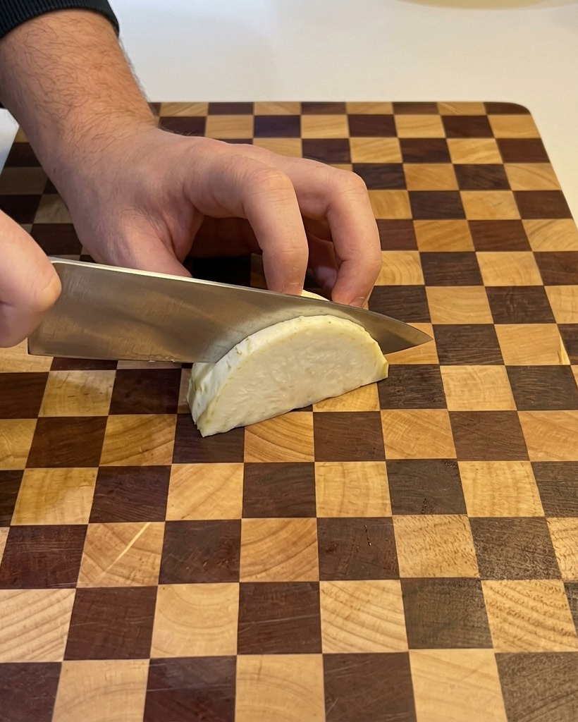 A person using a chefs knife to dice a wedge of white onion on a checkered wooden cutting board.