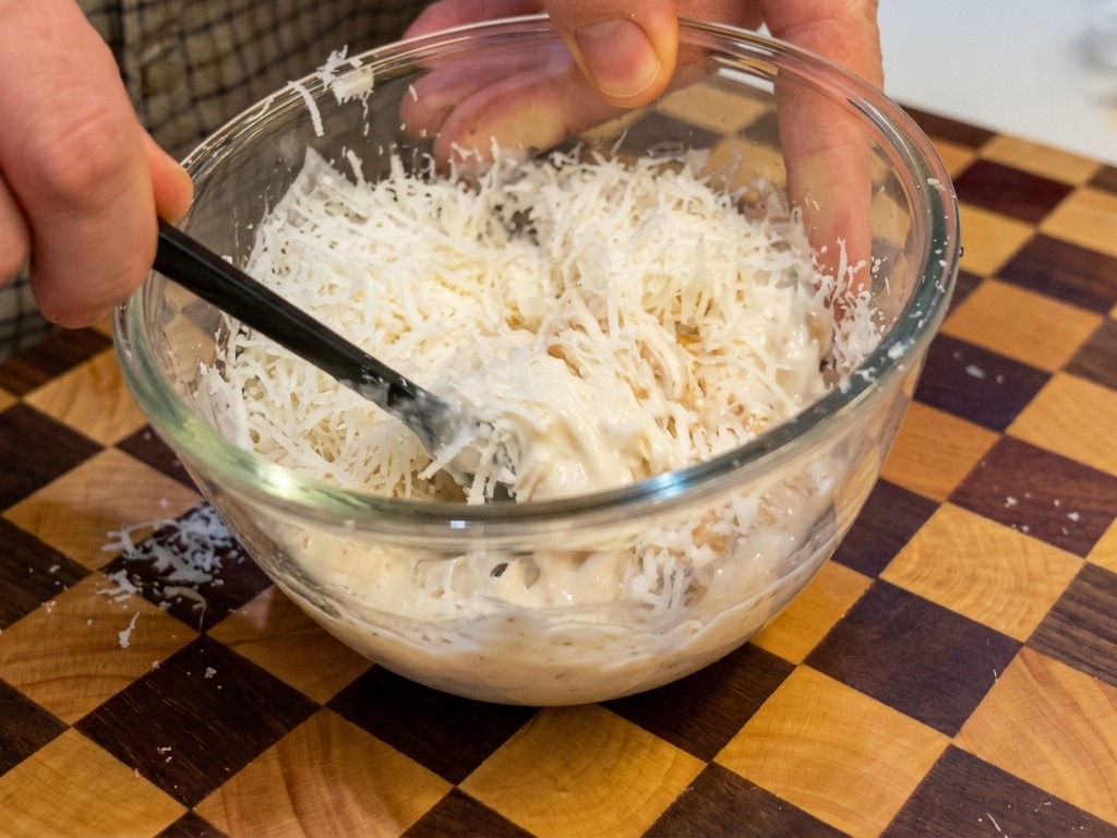 A thick, creamy pale-yellow mixture of eggs and cheese being stirred with black chopsticks in a clear bowl.