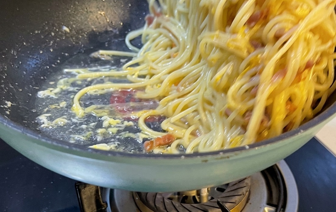 A beautifully plated serving of spaghetti carbonara on a white ceramic plate topped with grated cheese and pepper.