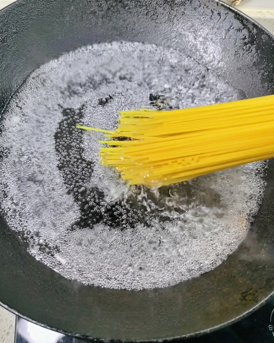 Dry spaghetti being lowered into a pot of vigorously boiling water.