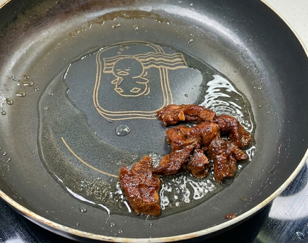 Marinated pork strips being sautéed in a pan with oil, showing a rich brown color and glossy surface as they cook.