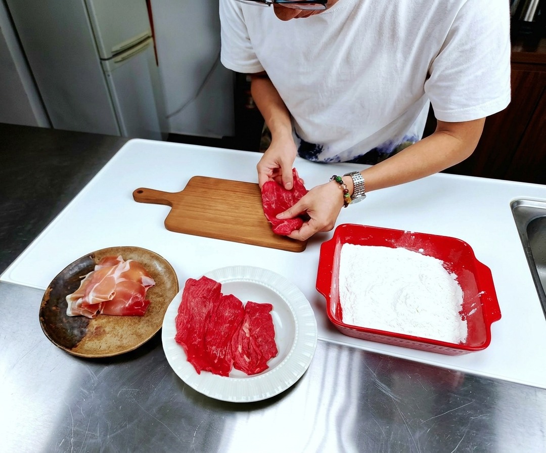 Thin slices of raw red veal laid flat on a light-colored wooden cutting board on a stainless steel counter.
