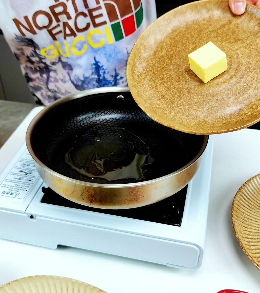 A knob of yellow butter being placed into a stainless steel frying pan already containing a pool of olive oil.