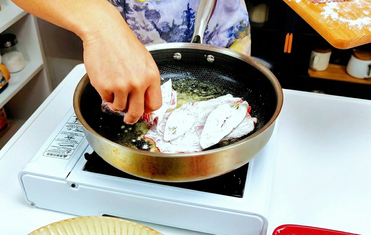 Hands placing flour-dusted veal slices into a hot pan with melted butter.