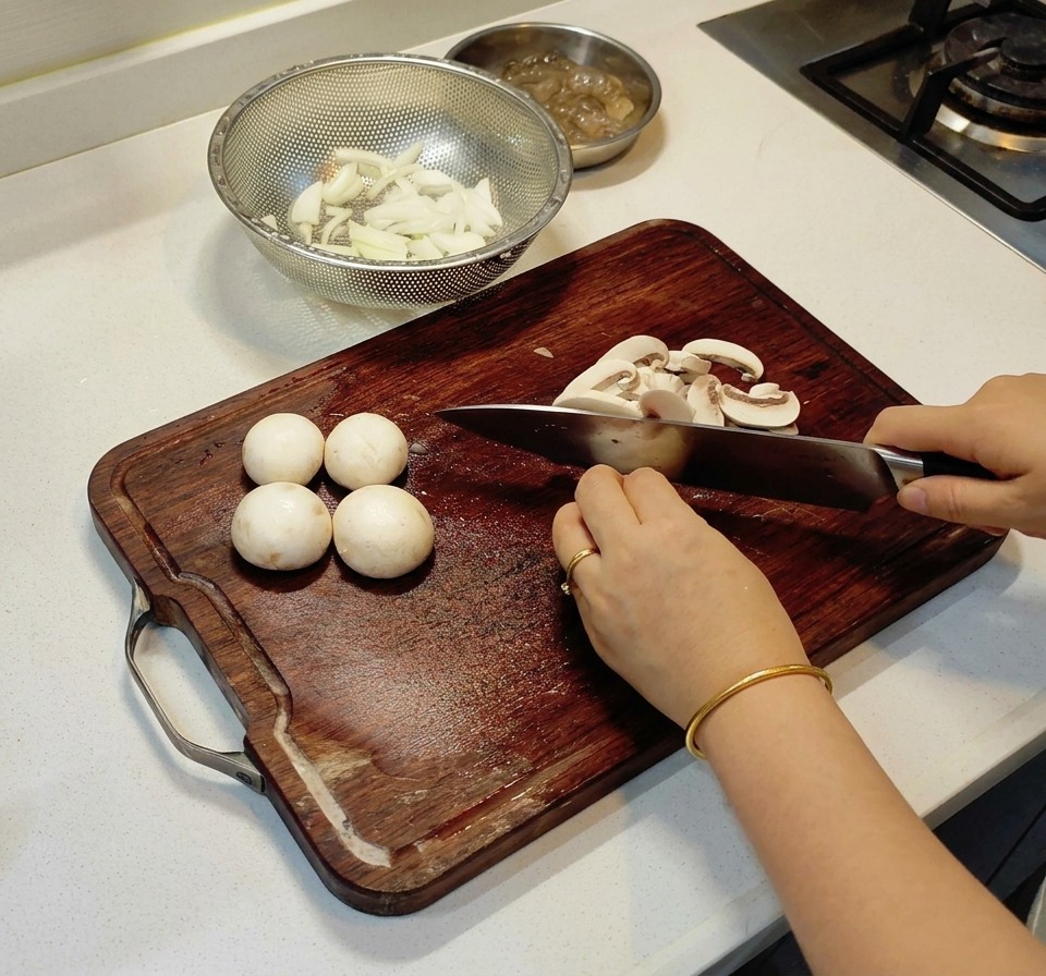 A person slicing white button mushrooms into thin strips on a wooden board.