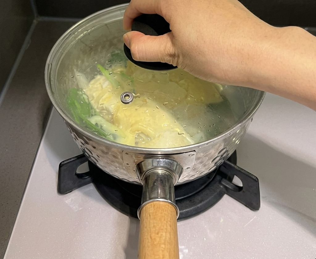 A hand placing a glass lid onto a pot of noodles and cheese to trap steam.
