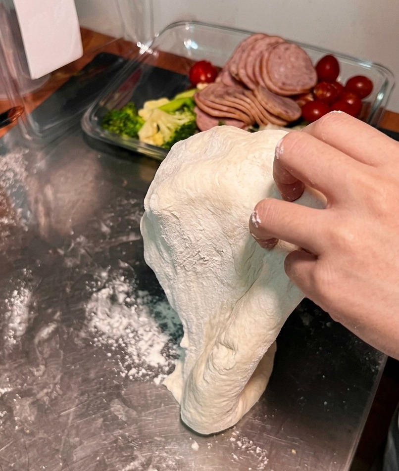 Pizza dough being stretched over the backs of two hands to increase its diameter and thinness.