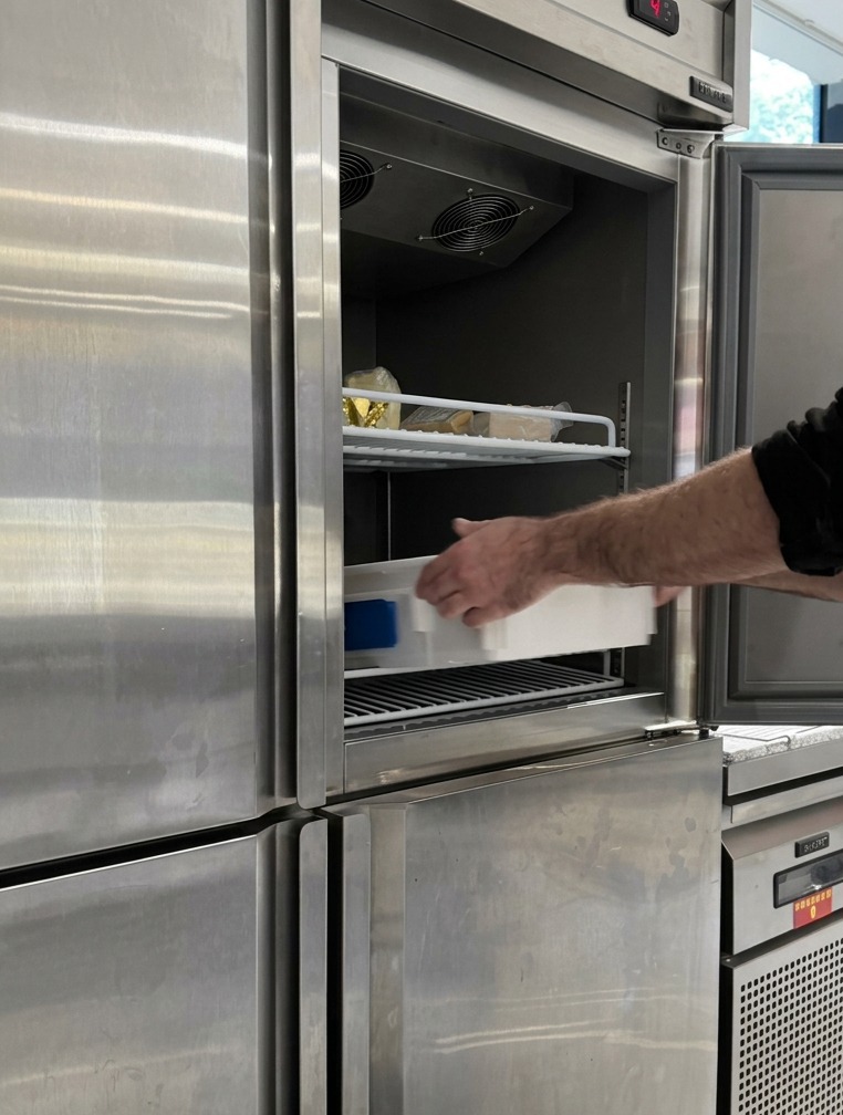 A white proofing tray filled with rounded dough balls being slid onto a shelf inside a professional stainless steel refrigerator.