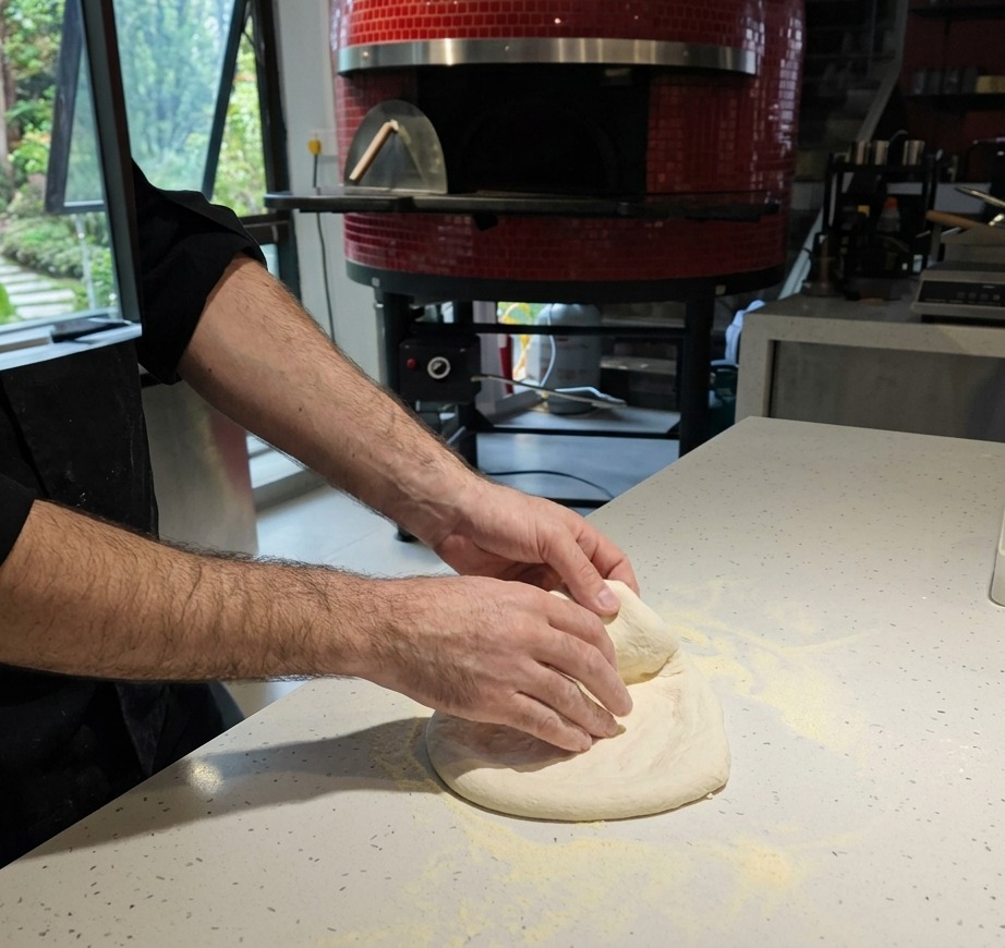 A close-up of hands stretching raw pizza dough on a flour-covered white countertop.