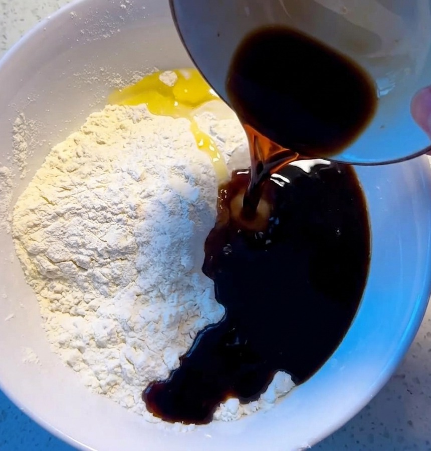 A person pouring liquid into a white bowl of flour and stirring with wooden chopsticks to create a shaggy pizza dough.