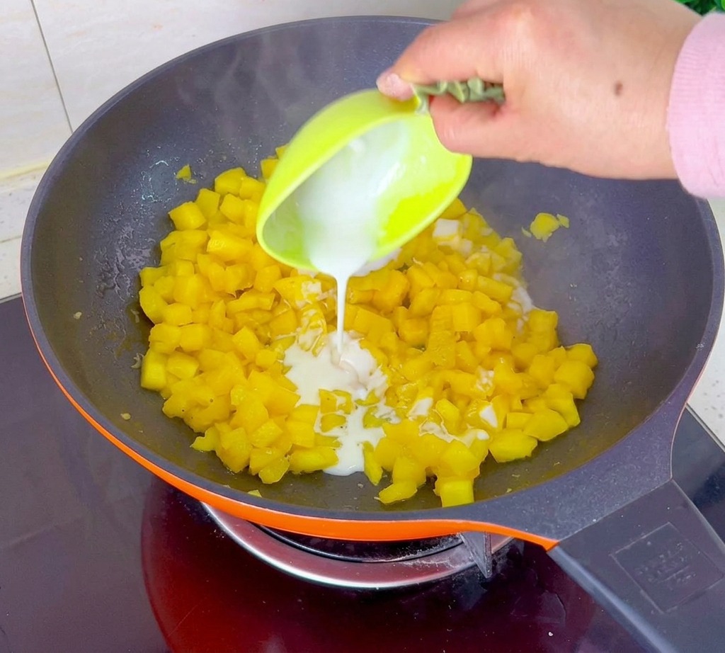 A white cornstarch mixture being poured from a lime green bowl into an orange pan filled with simmering diced pineapple.
