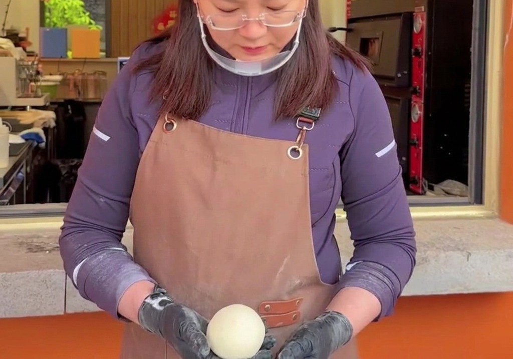 Hands carefully cupping and rotating a smooth, round ball of raw pizza dough to create surface tension.
