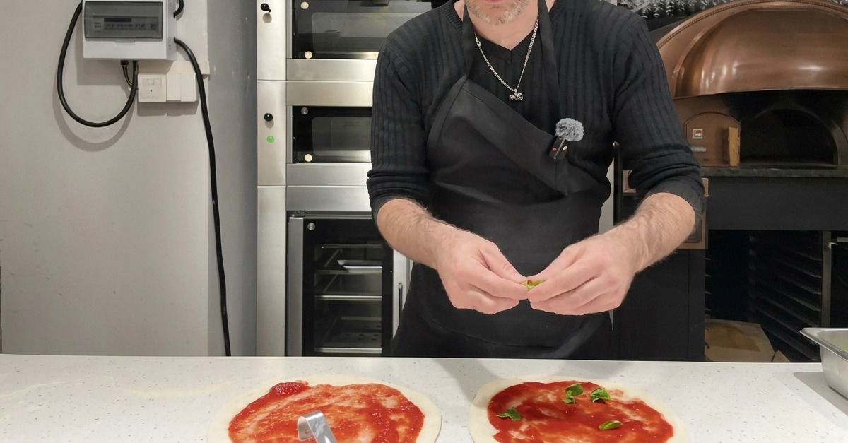 Fresh green basil leaves being carefully placed over a layer of tomato sauce on raw pizza dough.