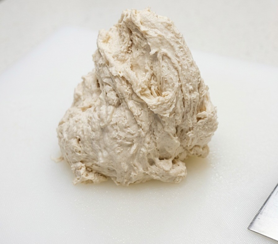 A mound of wet, shaggy pizza dough resting on a white plastic cutting board.