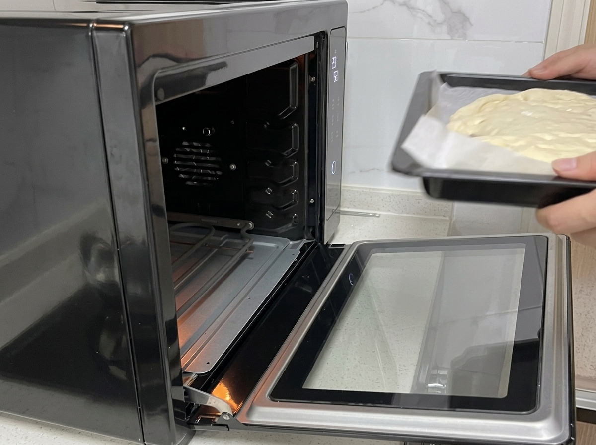 Hands sliding a baking tray with pizza dough into an open black oven.