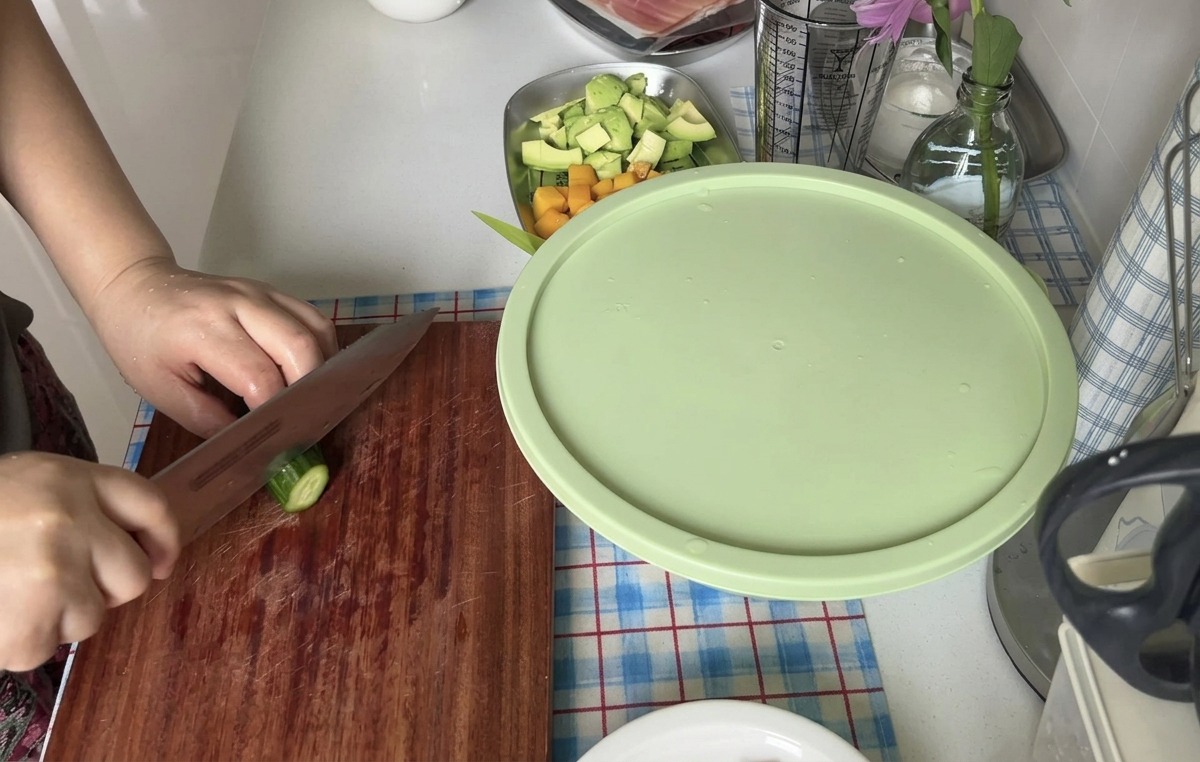 A person slicing a fresh cucumber into thin rounds using a sharp knife on a wooden board.