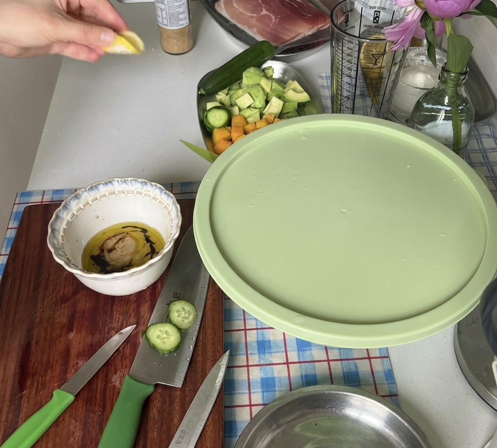 A hand squeezing juice from a fresh lemon wedge into a bowl containing salad dressing ingredients.