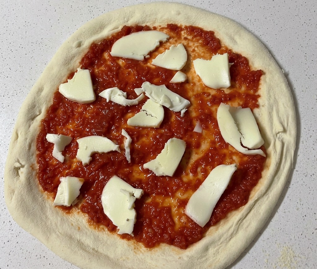 Hand-torn pieces of white fresh mozzarella cheese being placed onto a pizza base covered in red tomato sauce.