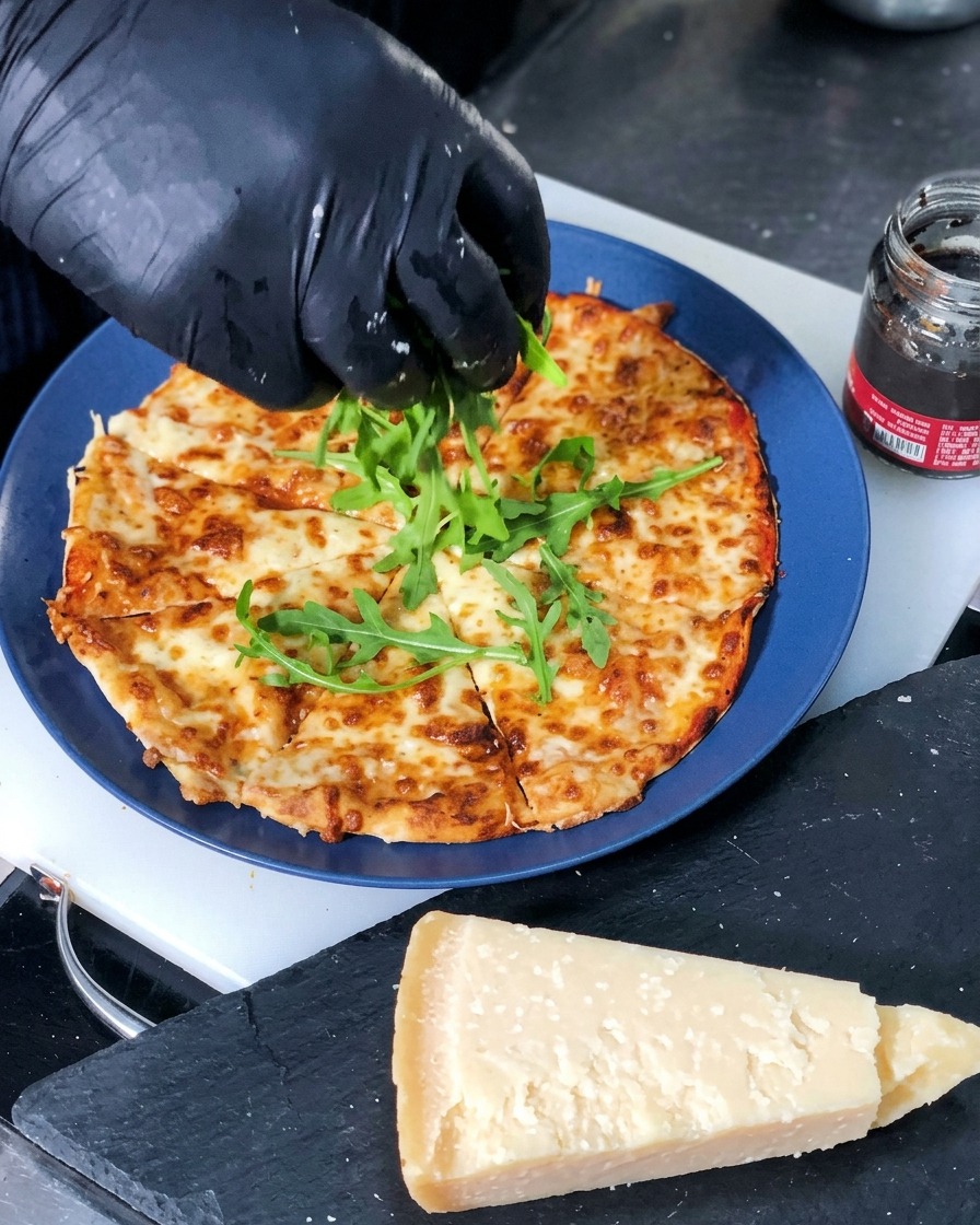 Fresh green arugula leaves being placed onto the center of a sliced, freshly baked cheese pizza.
