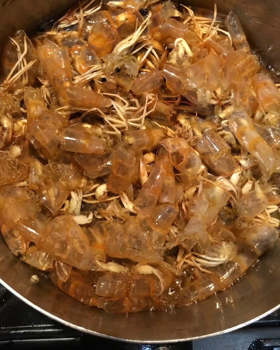 The shrimp shells simmering in a dark, liquid sauce mixture inside a pot.