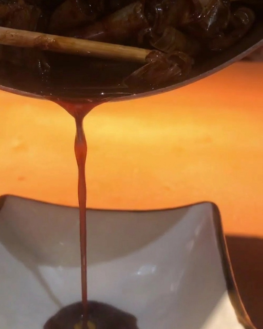 A dark, savory shrimp sauce being poured from a pot into a white square dish.