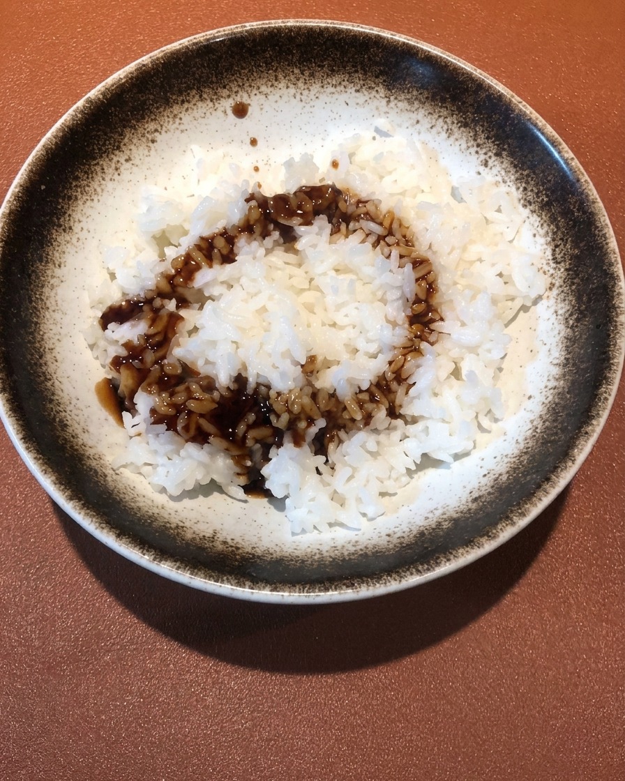 A close-up of dark, savory shrimp-infused sauce being poured onto a bowl of fluffy white rice.